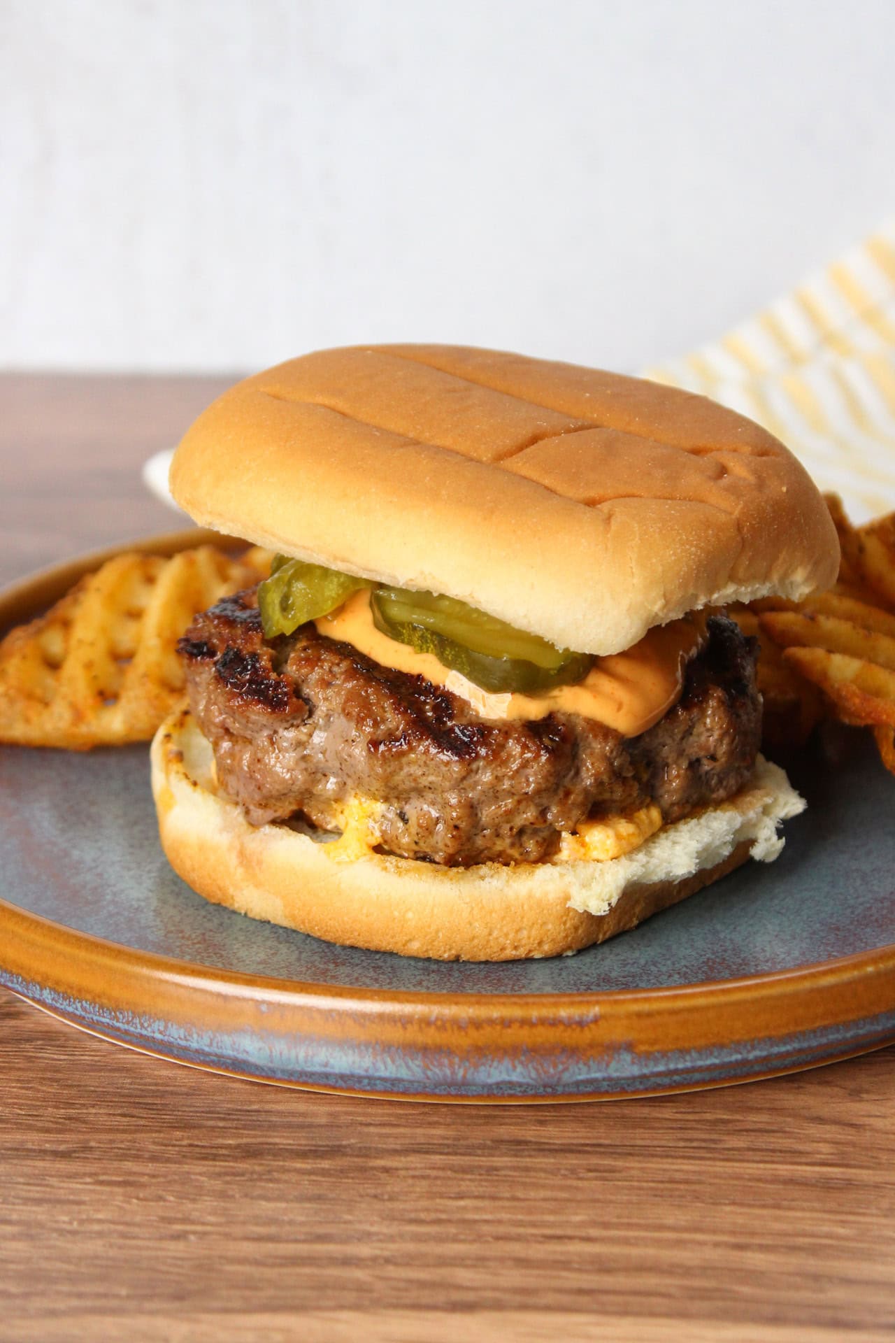 A cheese stuffed burger topped with sriracha mayo and pickles.