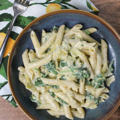 A bowl of pasta with spinach and artichoke cheese sauce.