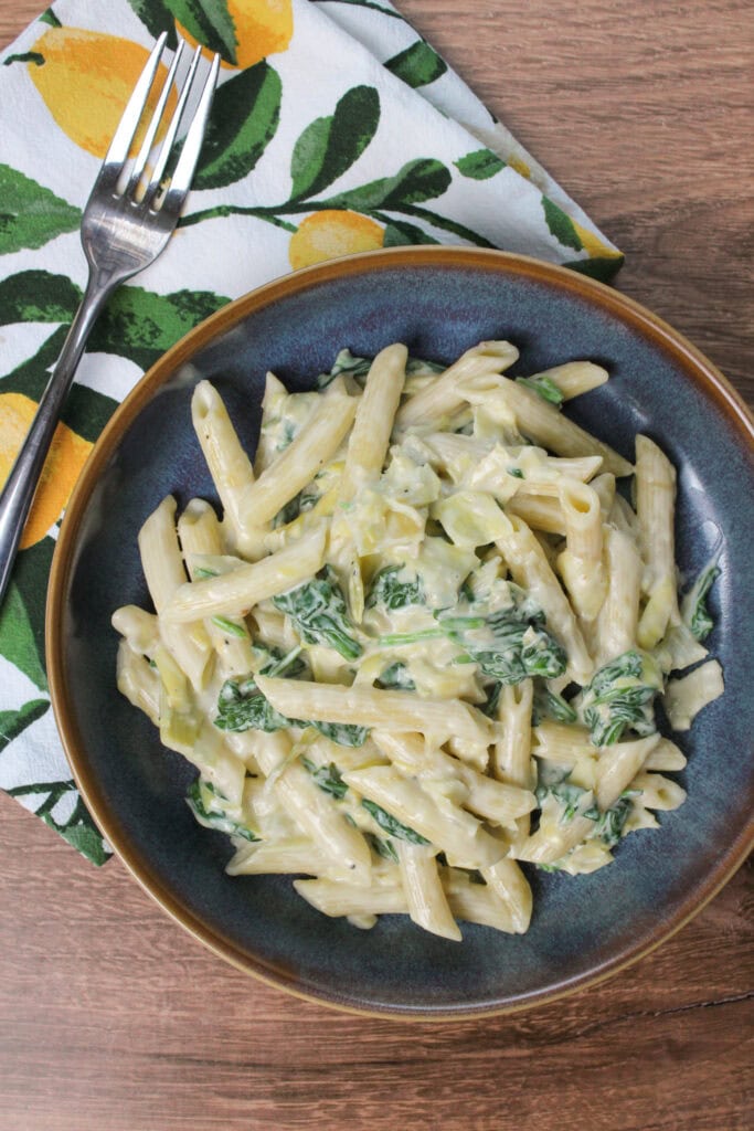 A bowl of pasta with spinach and artichoke cheese sauce.