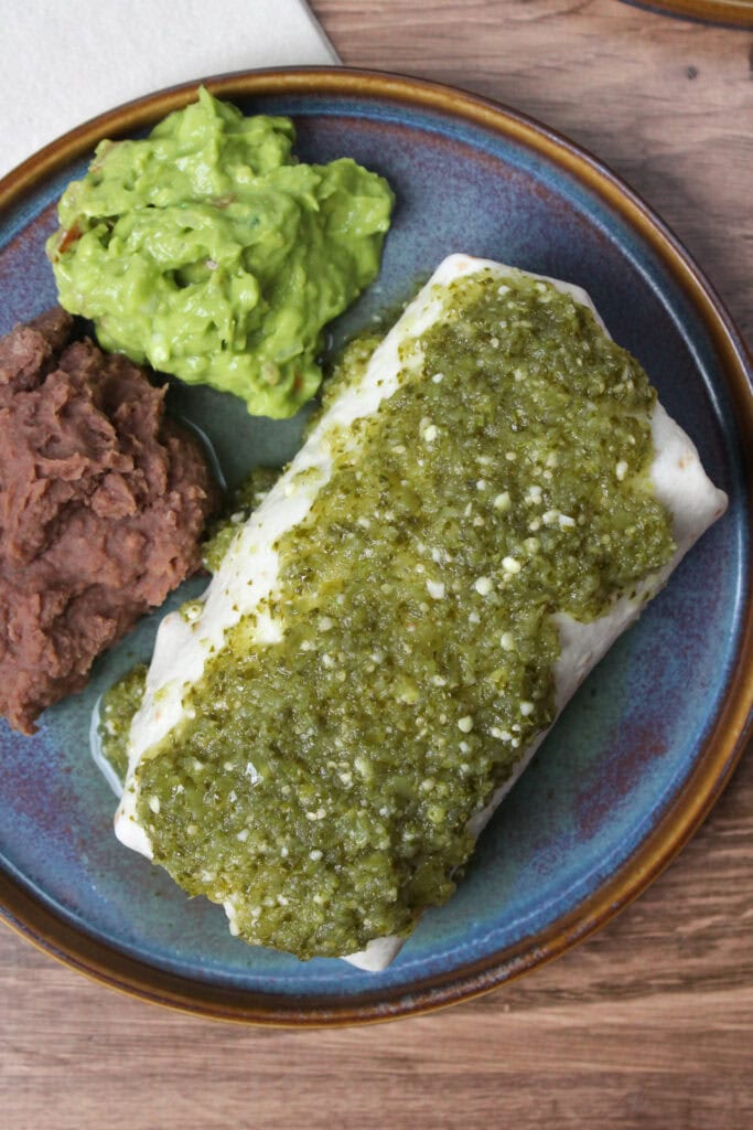 A carnitas burrito topped with verde sauce.