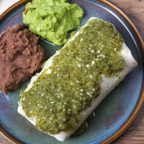 A wet burrito with salsa verde, served with refried beans and guacamole.