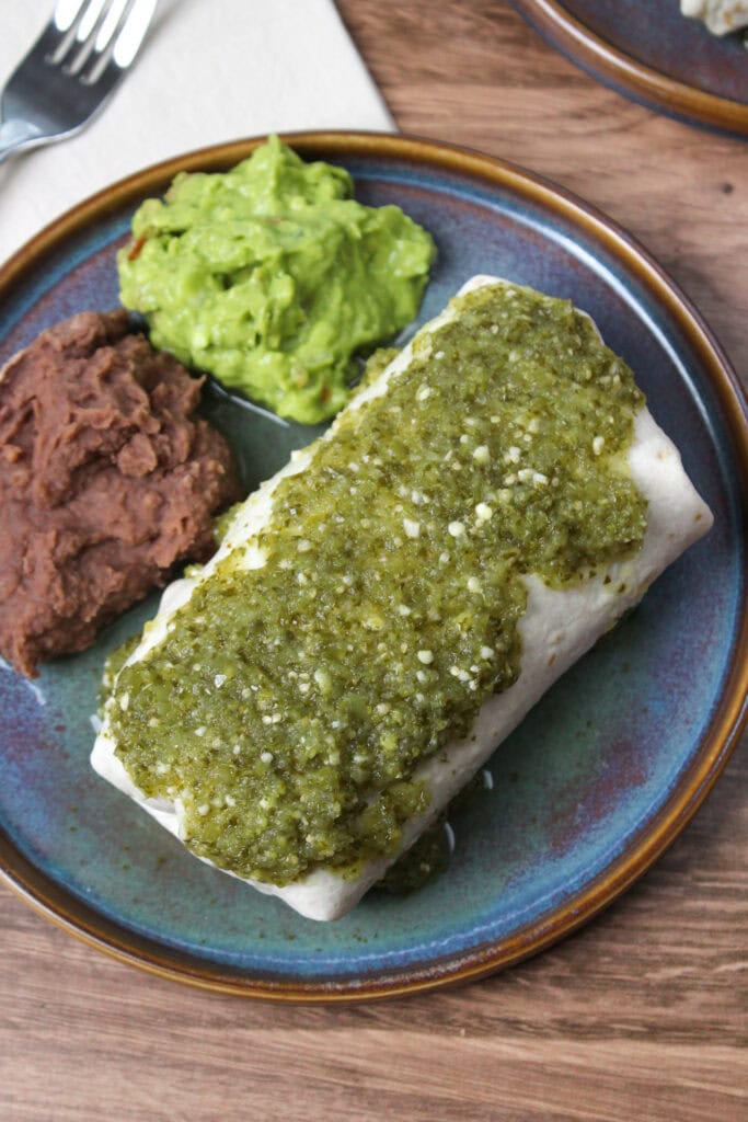 A wet burrito with salsa verde, served with refried beans and guacamole.