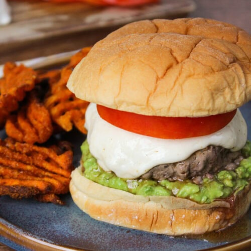 A burger with tomato, mozzarella, and avocado.