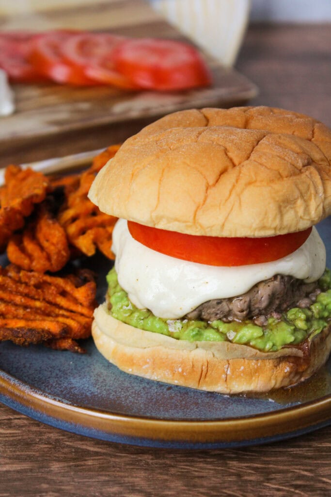 A burger with tomato, mozzarella, and avocado.