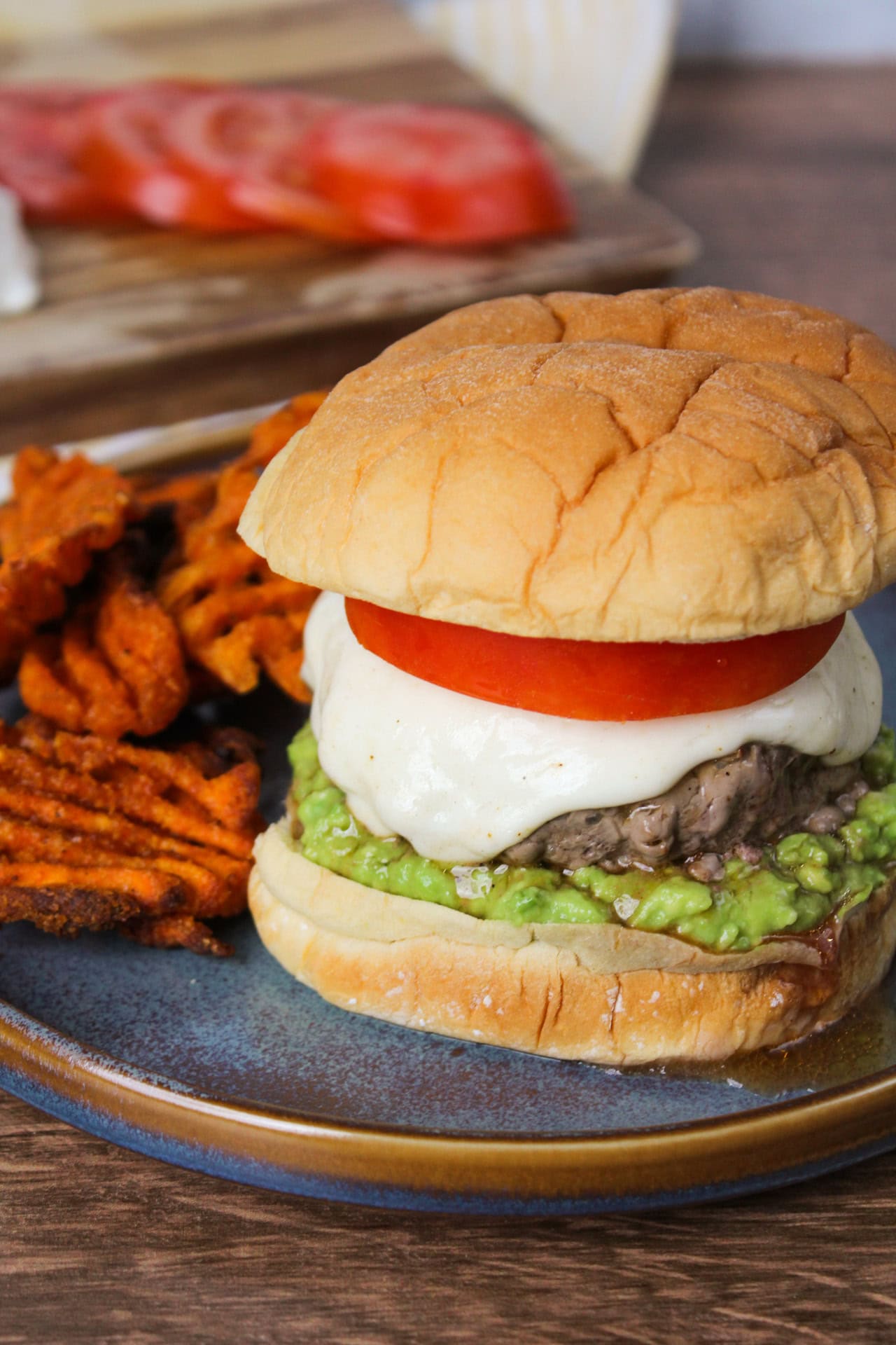 A burger with tomato, mozzarella, and avocado.