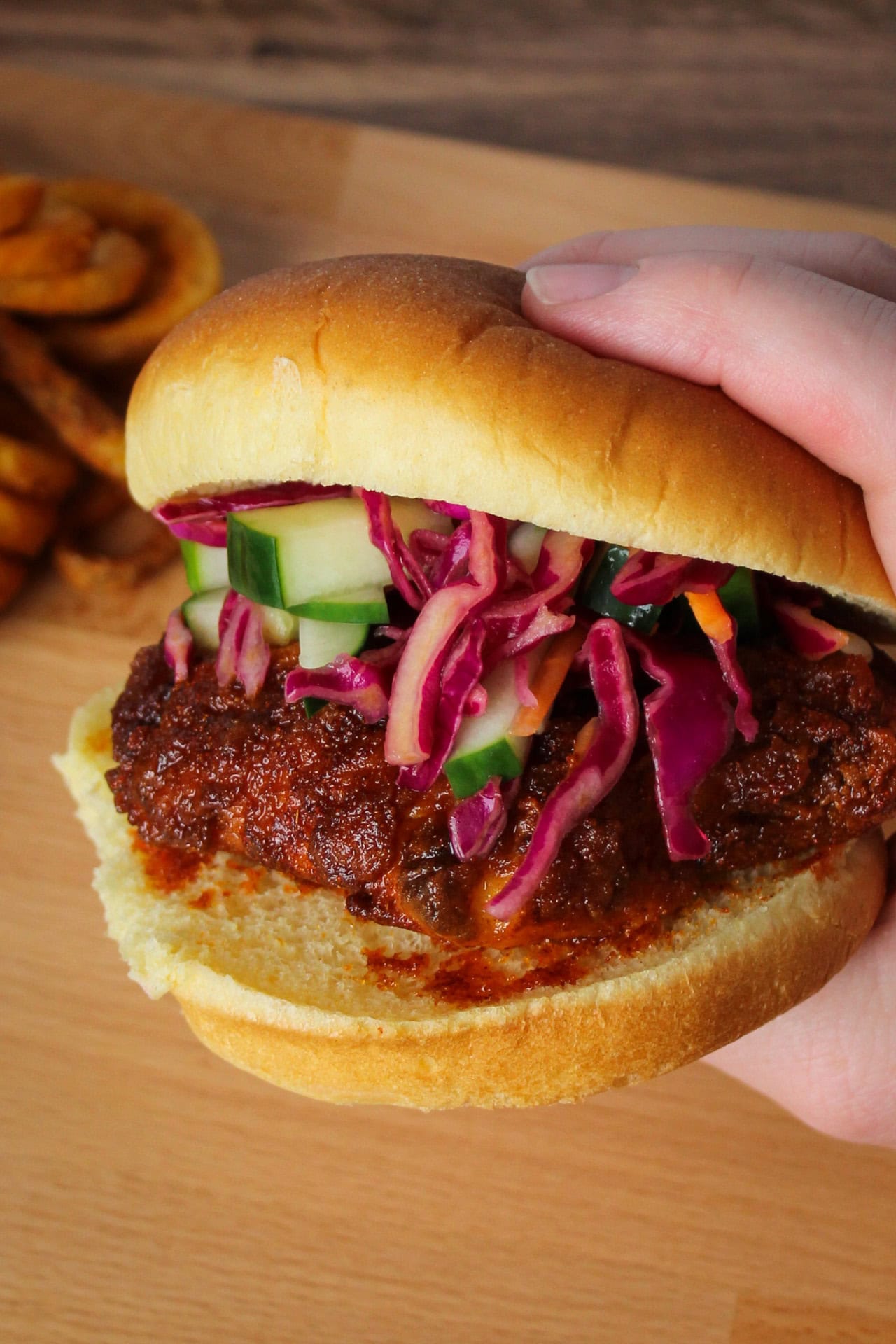 A Nashville hot chicken sandwich with a fiery sauce and crunchy pickled slaw on a potato bun being held.