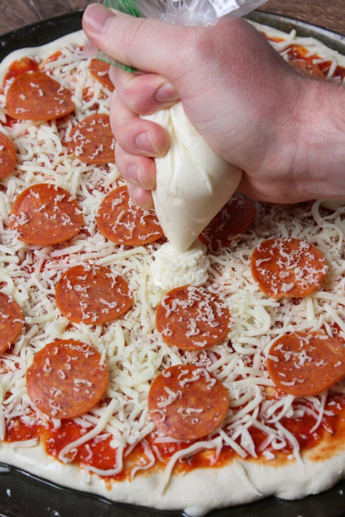 Piping ricotta onto a pepperoni pizza before it bakes.