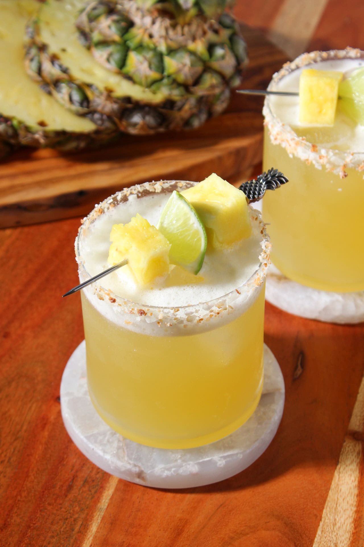 Tropical coconut pineapple margaritas in rocks glasses garnished with a toasted coconut rim and a pineapple and lime wedge skewer. 