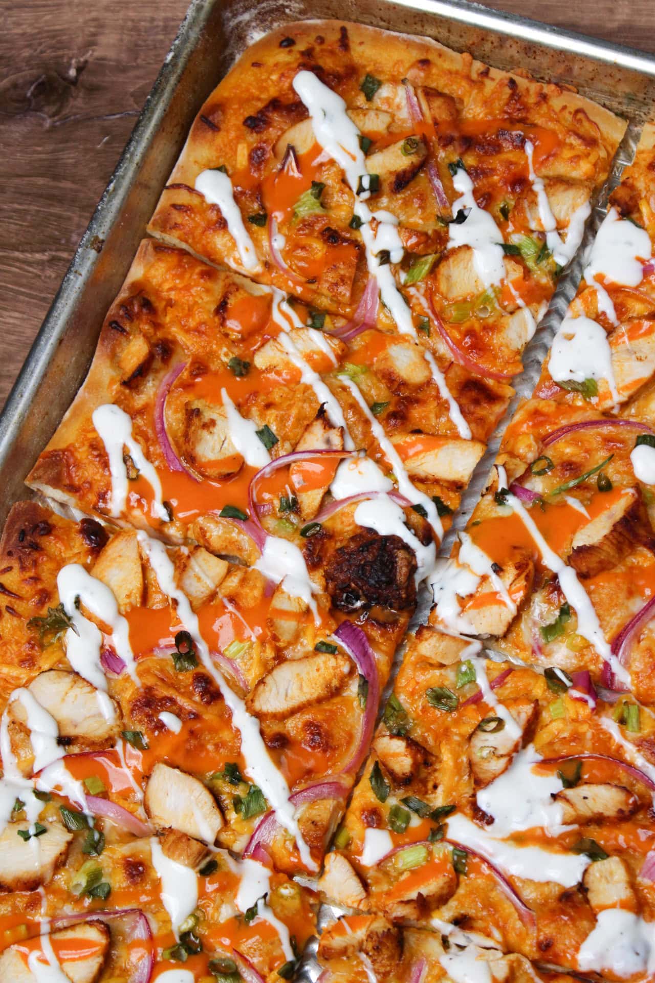 Spicy buffalo chicken pizza sliced in rectangles on a sheet pan.