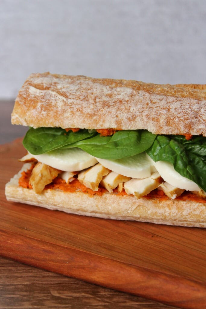 A sandwich with sun dried tomato pesto, chicken, mozzarella, and spinach.