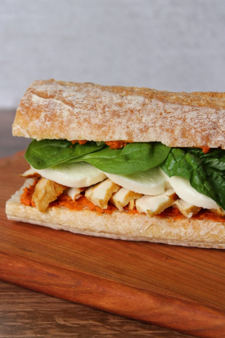 A sandwich with sun dried tomato pesto, chicken, mozzarella, and spinach.