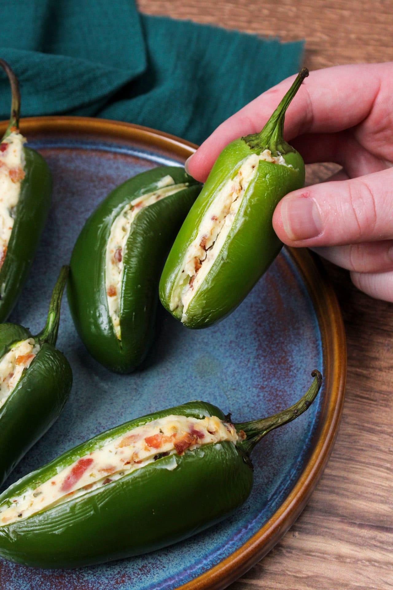 A Jalapeno popper with bacon cream cheese filling being held over a plate of more of them.