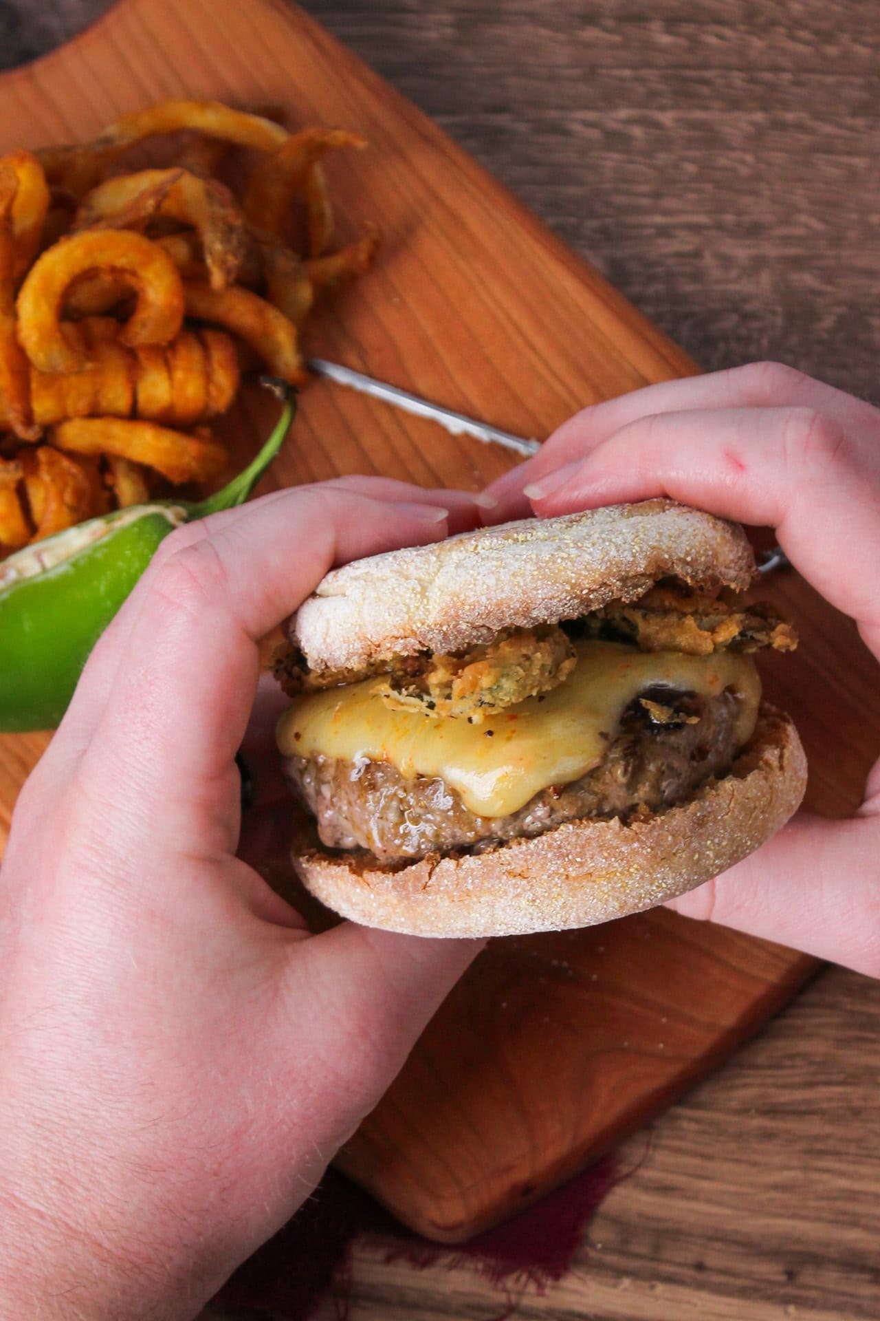 Jalapeno cheeseburger on an english muffin being held.
