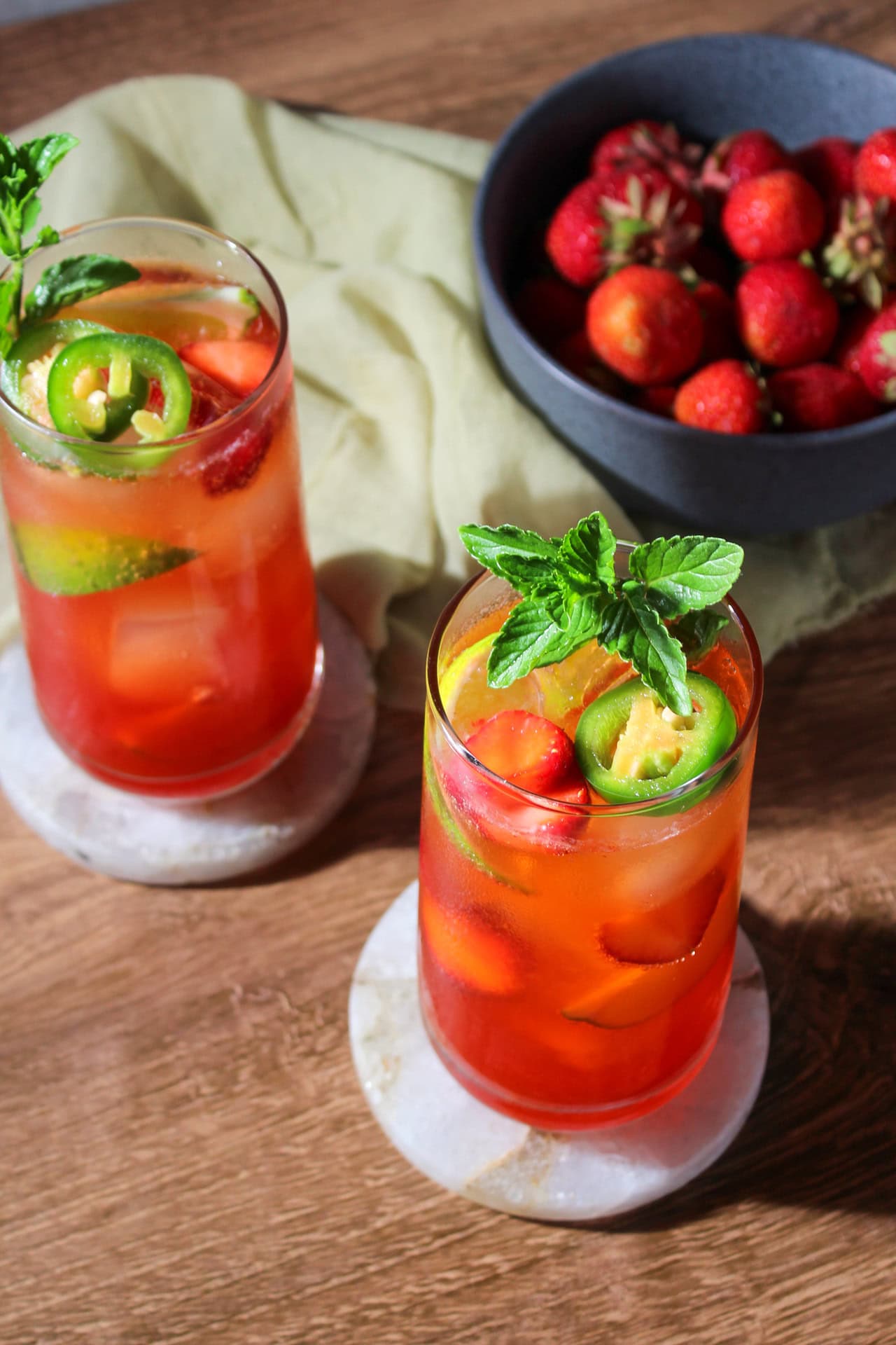 Two strawberry jalapeno mojitos garnished with jalapeno, lime, strawberries, and mint in collins glasses. 