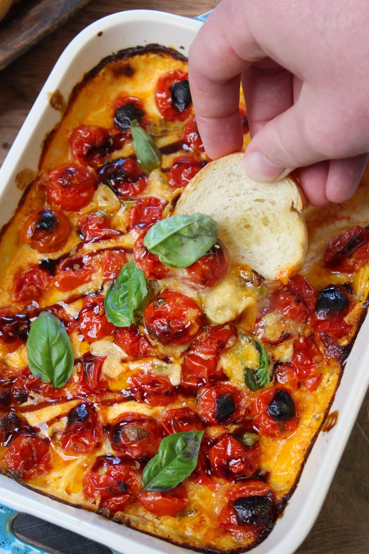 A crostini scooping up some cheesy baked bruschetta dip.