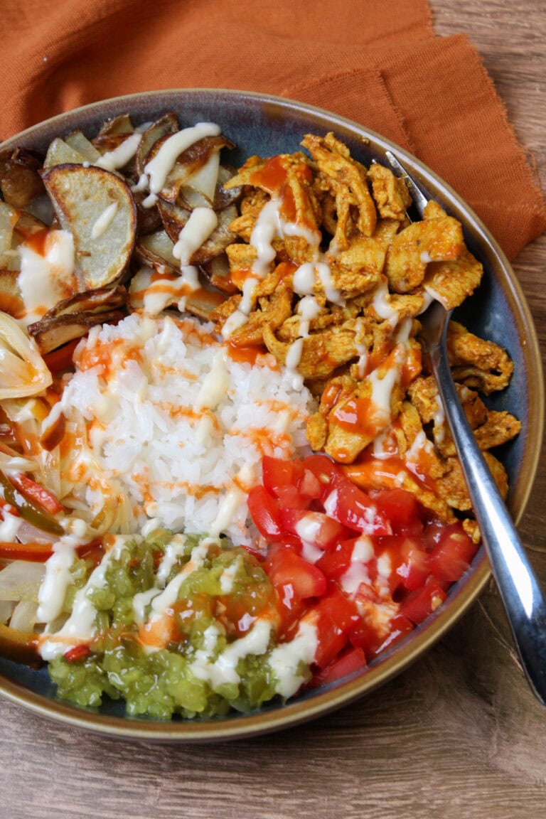 A chicken shawarma bowl with rice, tomatoes, pickle relish, potatoes, and garlic aioli.