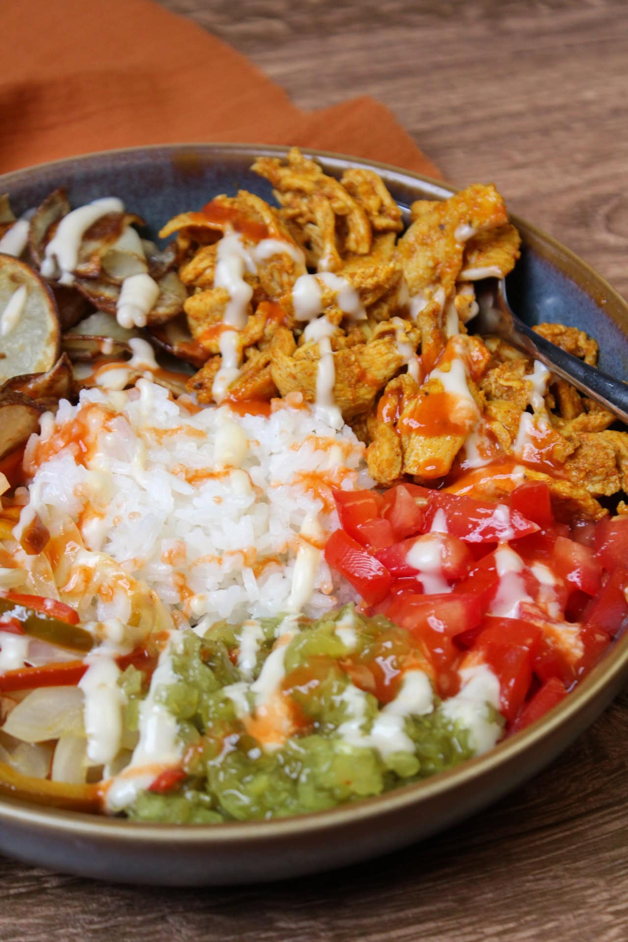 Chicken shawarma style rice bowl plated in sections and drizzled with garlic aioli. Bowl includes rice, tomato, pickle relish, chicken shawarma, crispy potatoes, and pepper and onion.