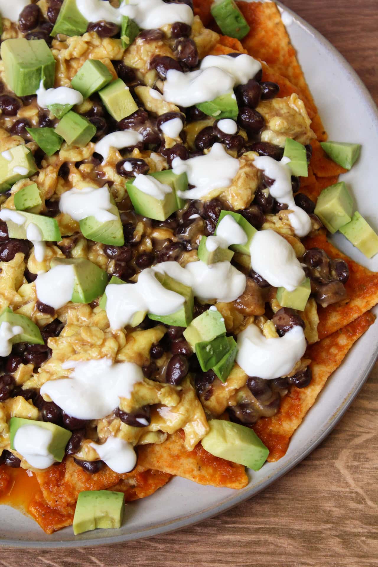 A plate of chilaquiles rojos with scrambled eggs made with black beans, cubed avocado, and crema.