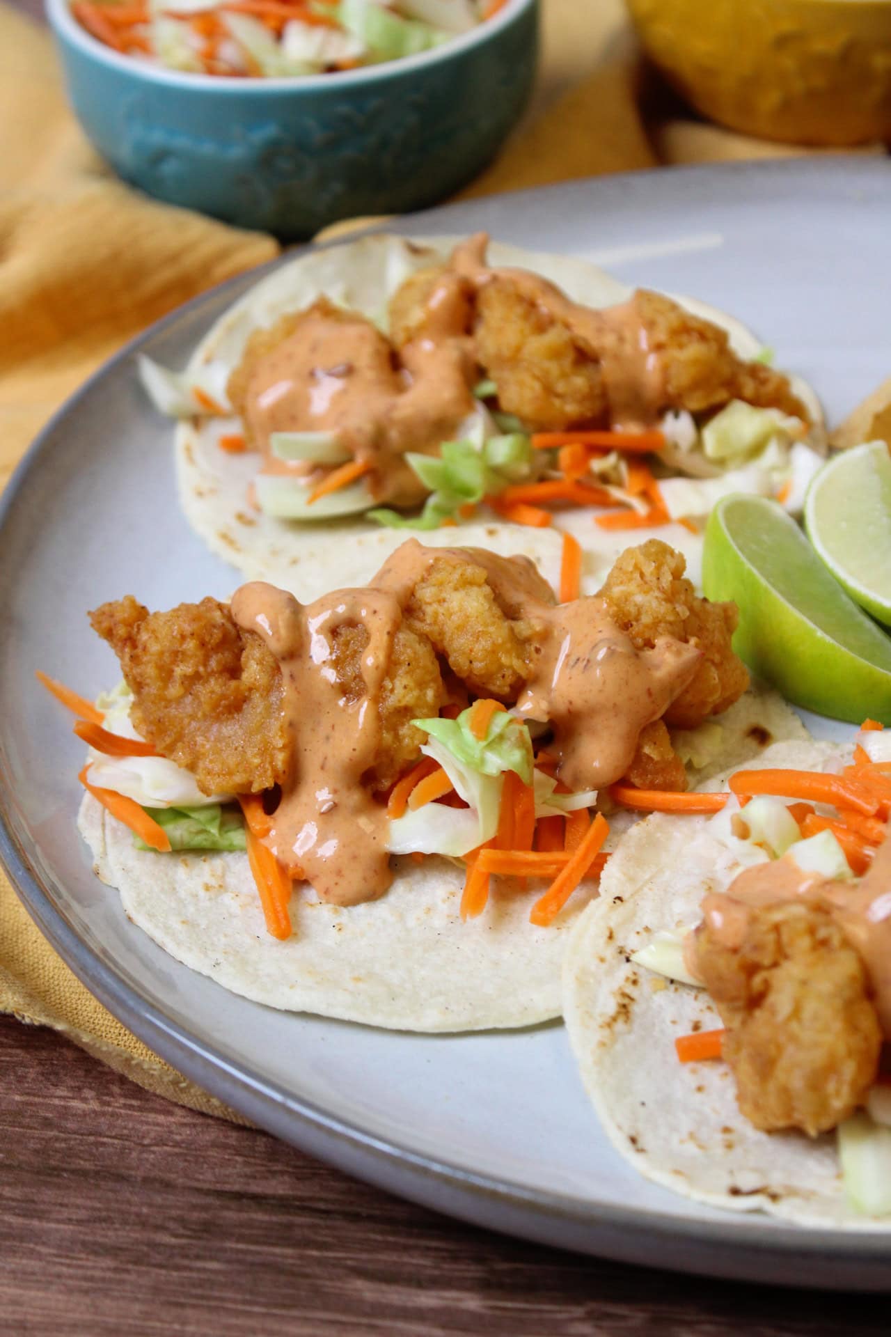 A plate of fried shrimp tacos, slaw, and chipotle mayo on corn tortillas. 