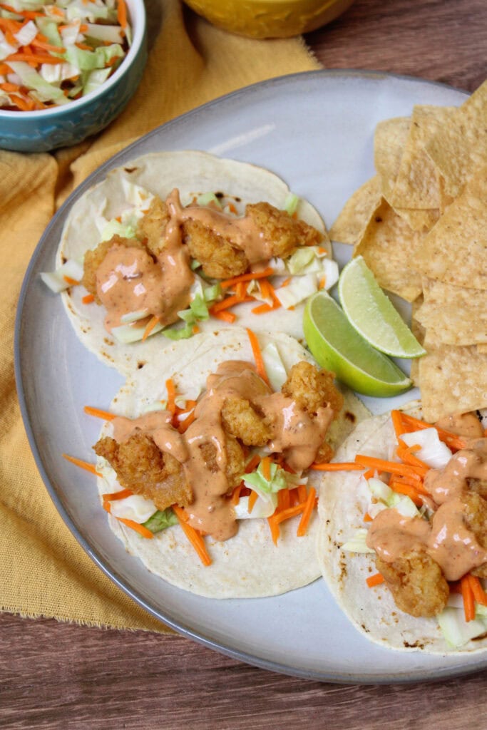 Crispy fried shrimp tacos on a plate with tortilla chips and lime wedges.