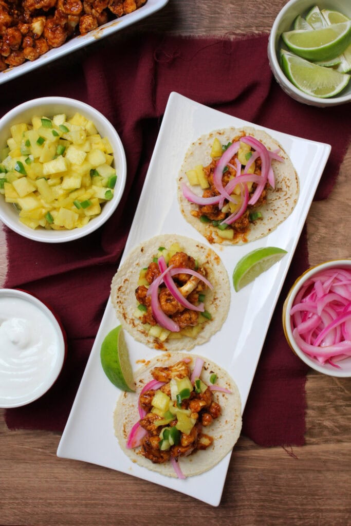 Three spicy cauliflower tacos with pineapple pico de gallo and pickled red onions.