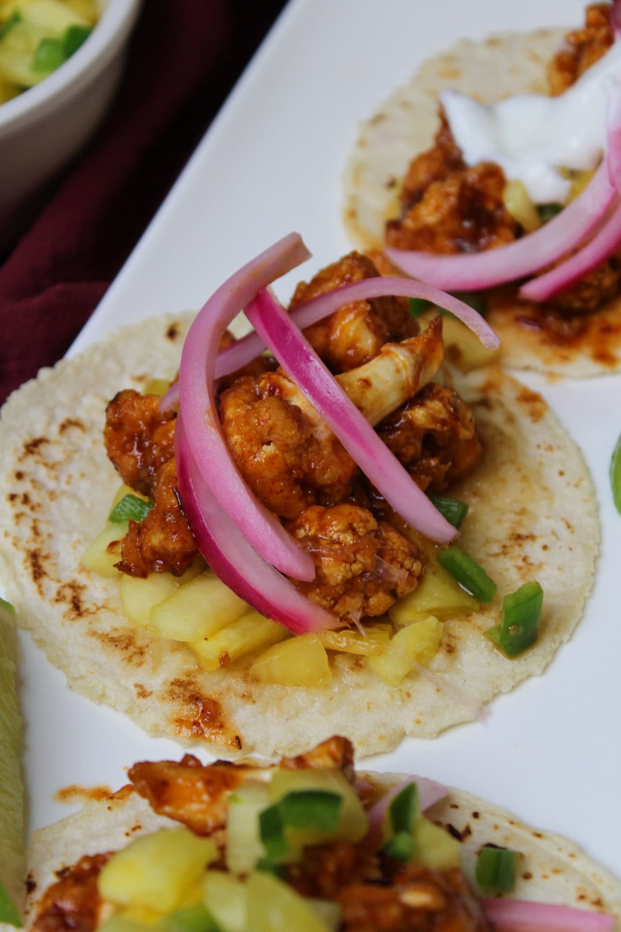 A close up of air fryer cauliflower tacos with spicy chipotle glaze, pineapple pico, pickled red onion, and a lime crema. 