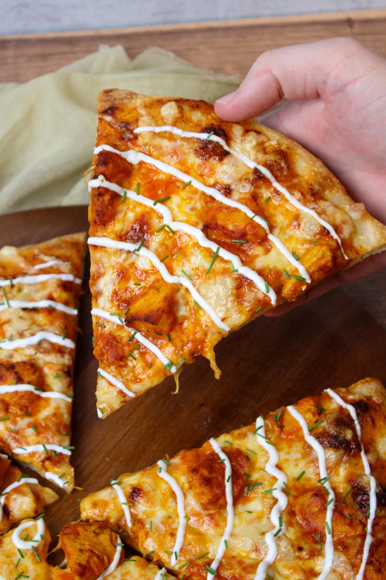 A slice of butter chicken pizza with a yogurt sauce drizzle being held over the rest of the pizza.