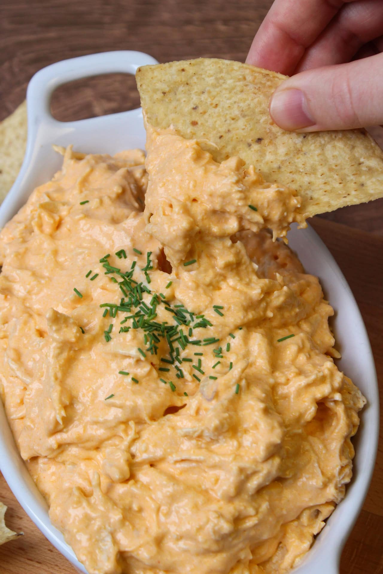 Dipping a chip into high protein buffalo chicken dip made with cottage cheese and topped with chopped chives.