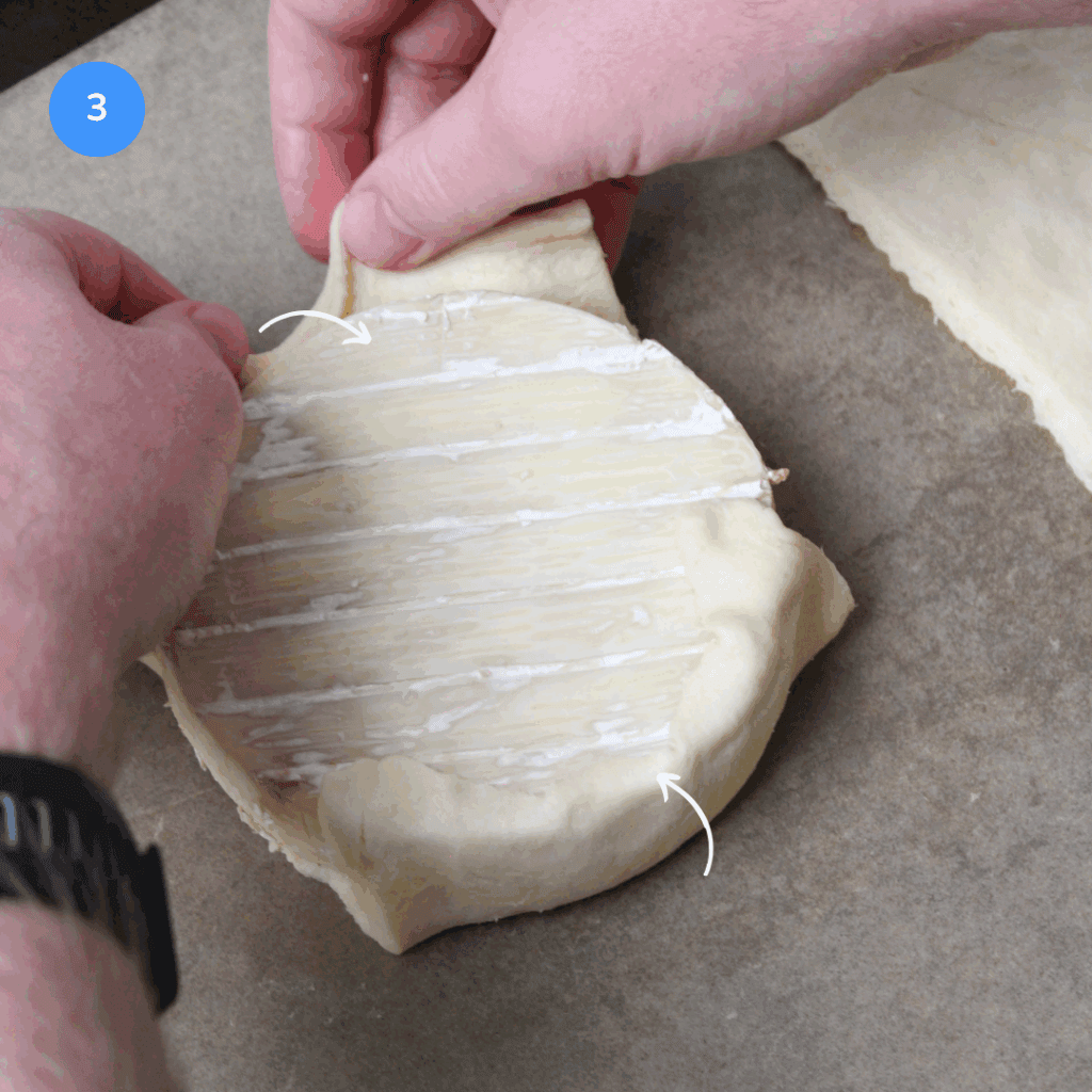 Folding pastry dough over a wheel of brie.