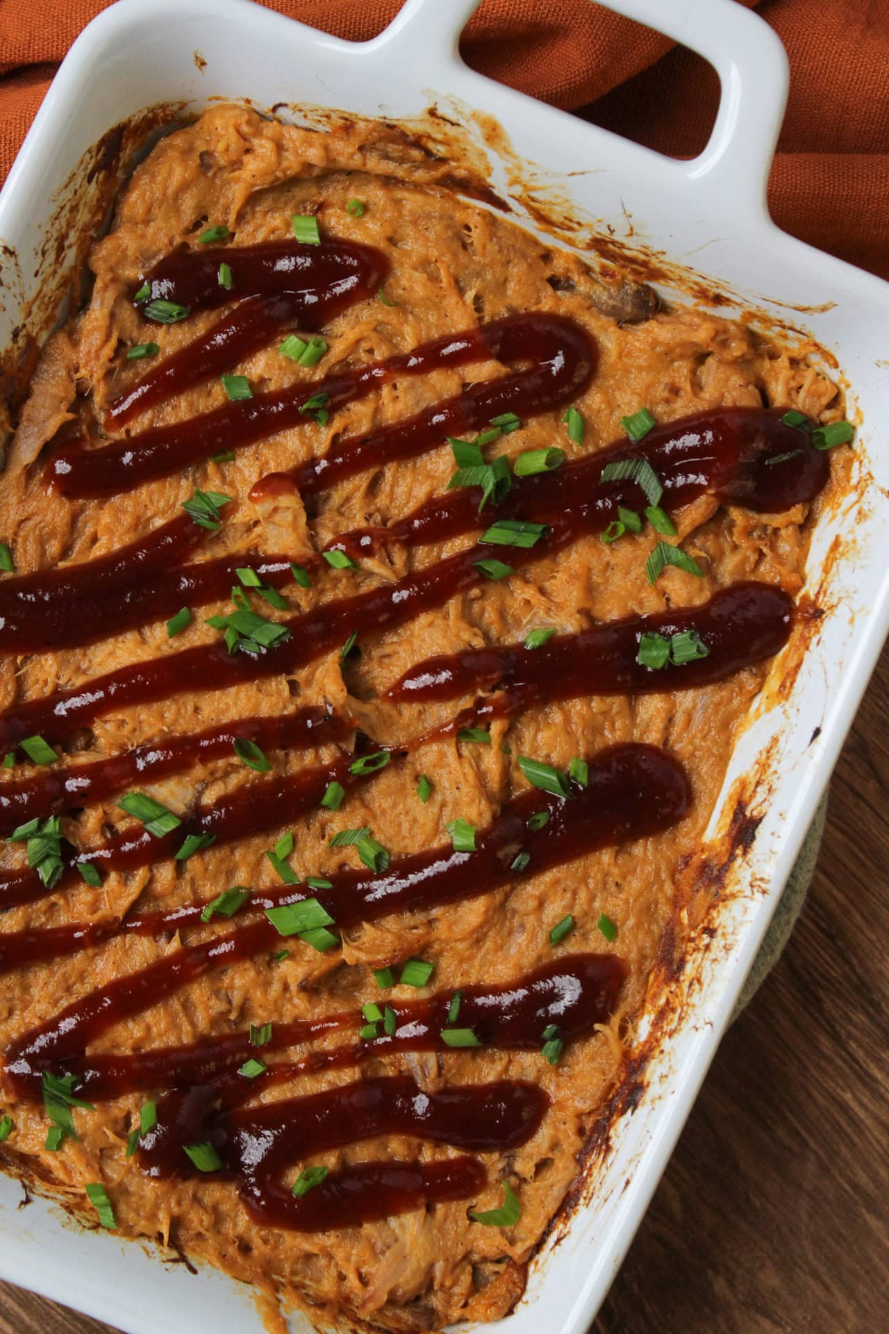 BBQ pulled pork dip topped with a drizzle of BBQ sauce and chopped chives in a white serving dish.