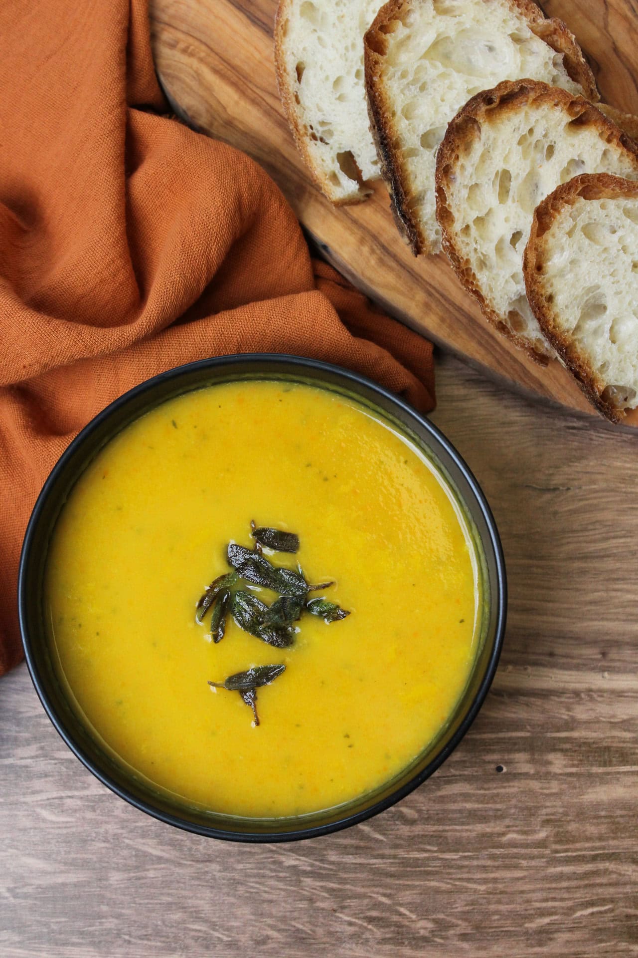 Butternut squash soup in a black bowl topped with crispy sage and served with bread.