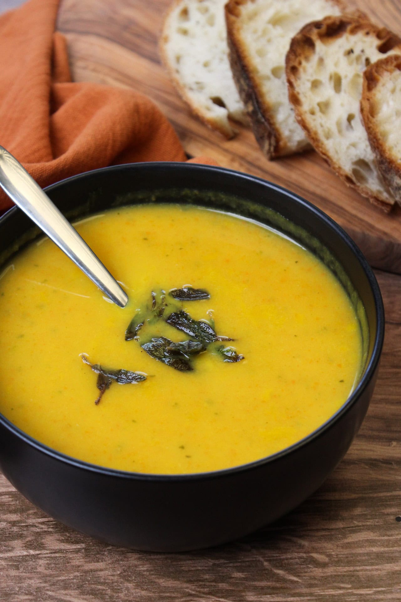 A black bowl of butternut squash and carrot soup topped with crispy sage.