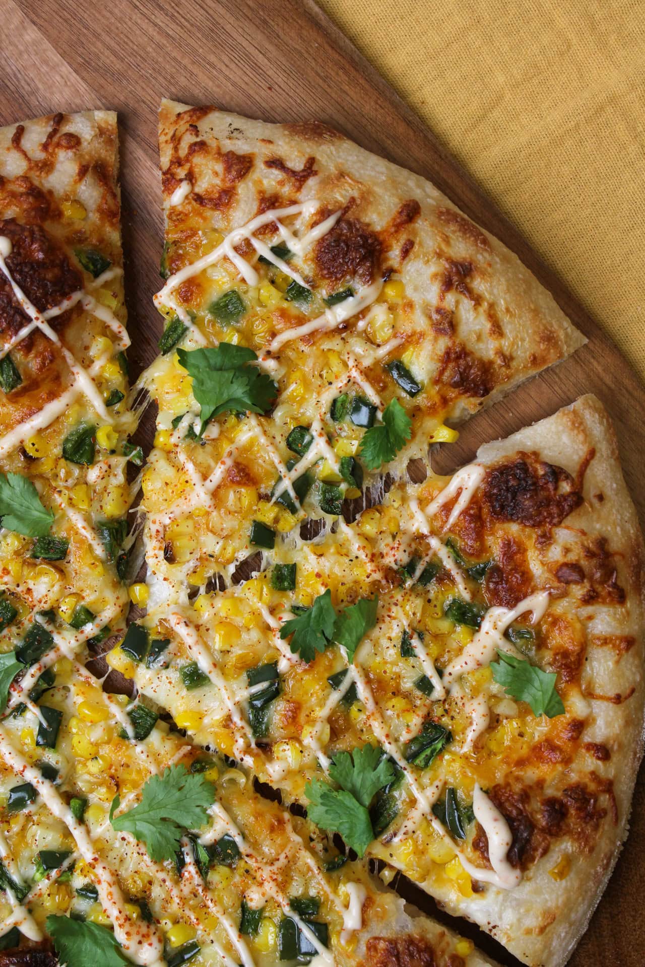 This elote pizza is topped with roasted corn, poblano pepper, bechamel, cheddar jack, mozzarella, and drizzled with a tajin lime aioli.