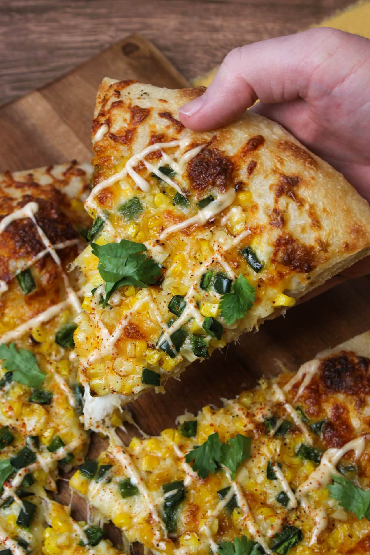 A slice of Mexican street corn pizza that is topped with roasted corn, poblano pepper, bechamel, cheddar jack, mozzarella, and drizzled with a tajin lime aioli.