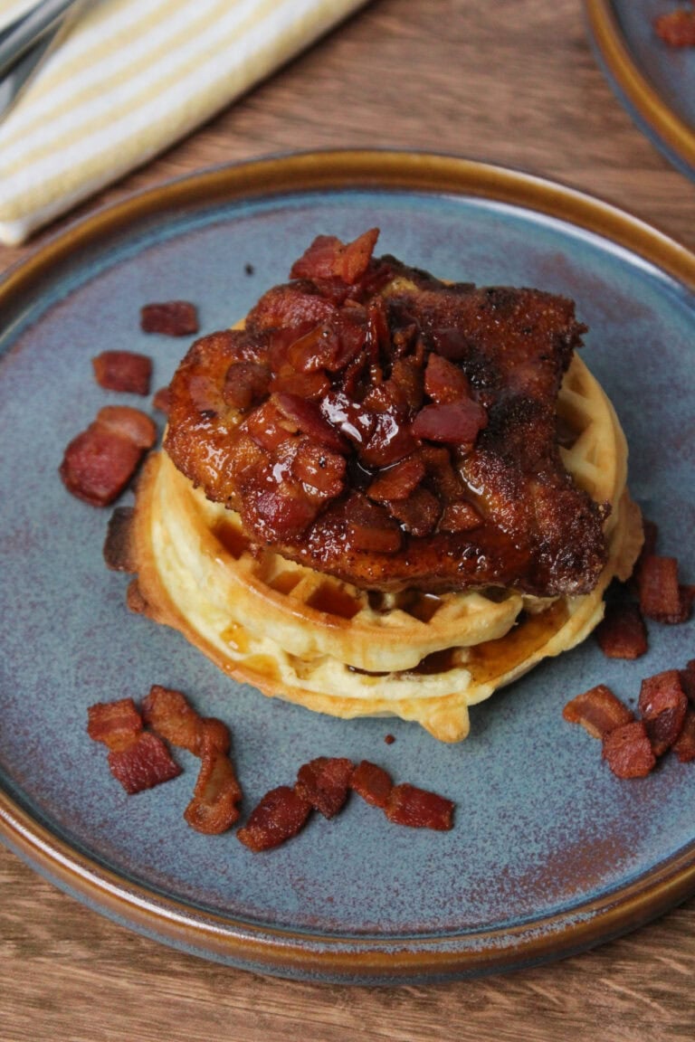 A plate of fried chicken and waffles topped with bacon.