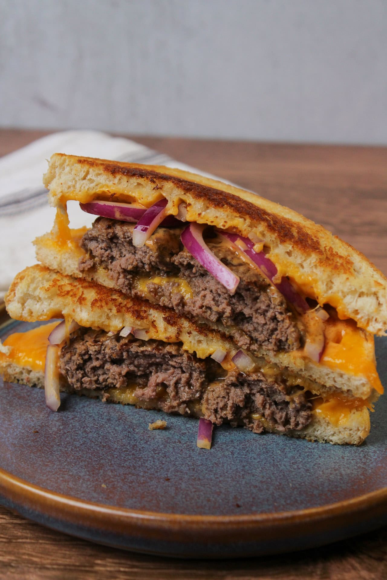 A grilled cheese burger made with cheddar cheese, sourdough, red onions, and chipotle mayo on a blue stoneware plate.