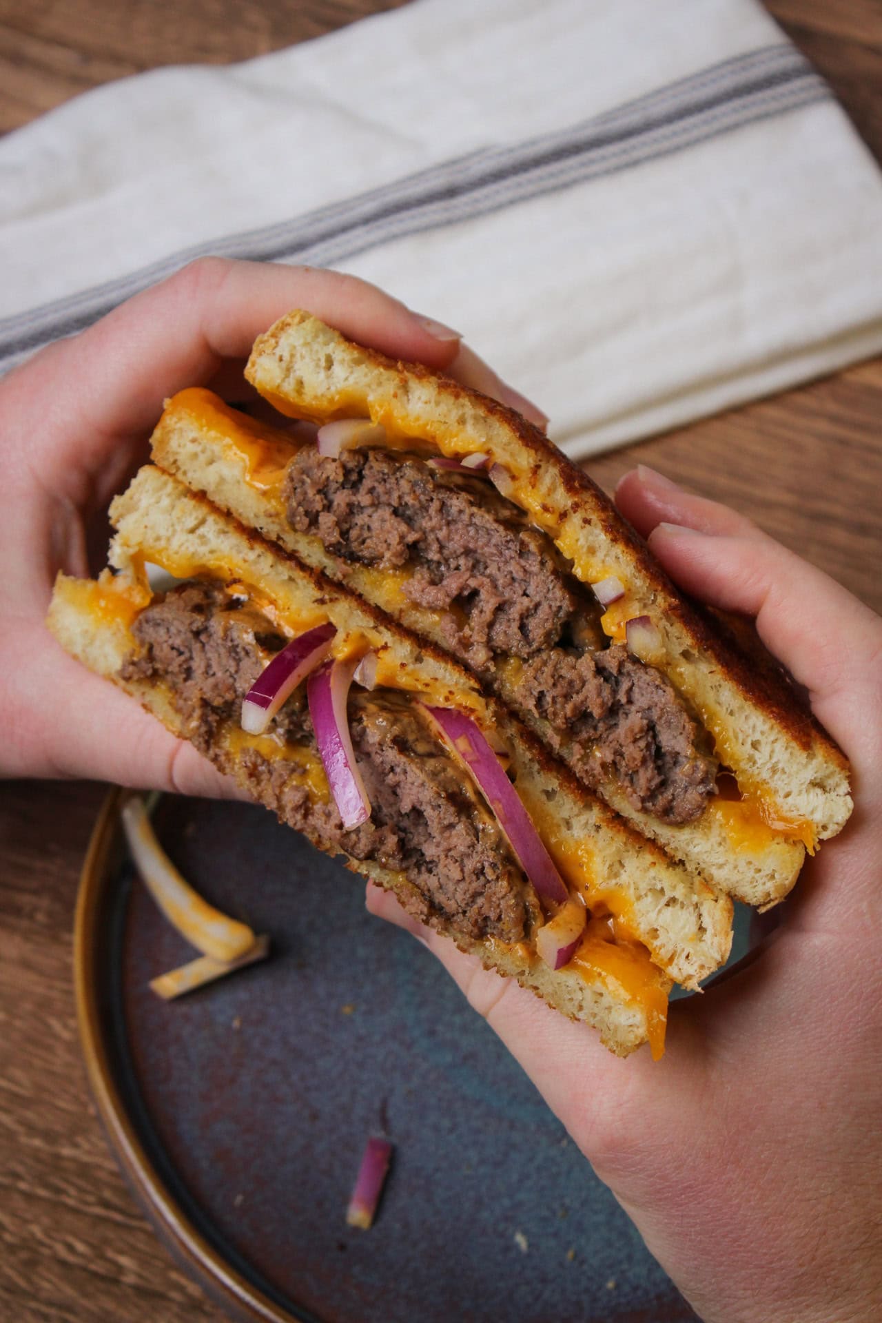 Two halves of a grilled cheese patty melt burger being held together to show off the inside. 
