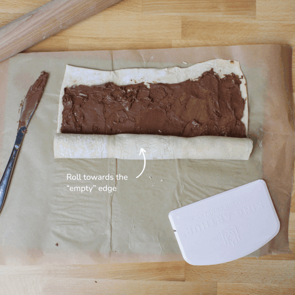 A partially rolled square of puff pastry with Nutella.