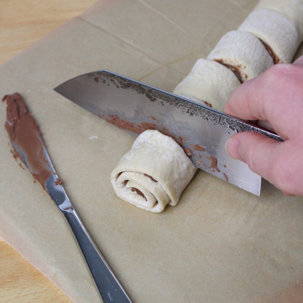 Slicing puff pastry with Nutella into swirls.