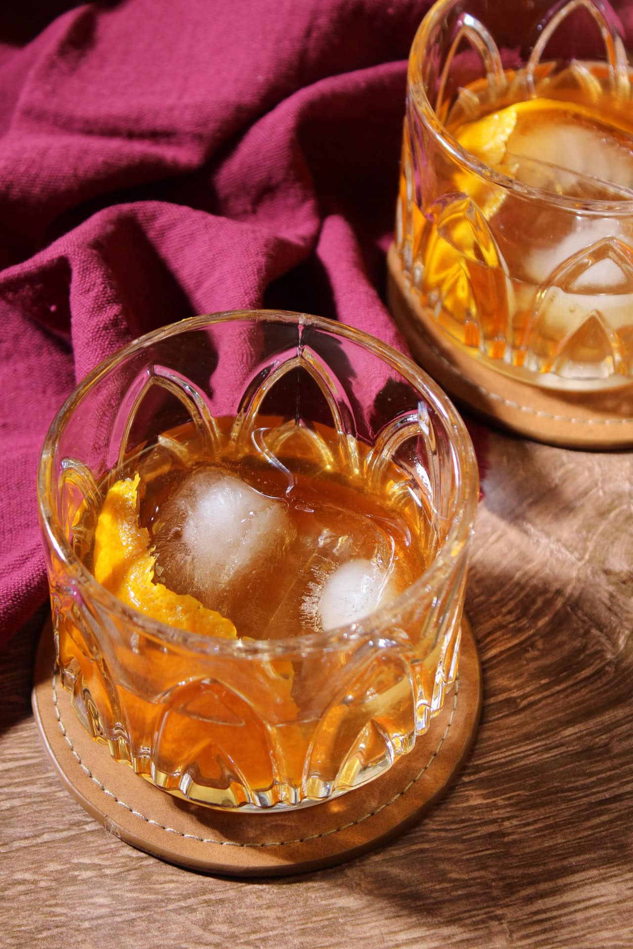 Two tequila old fashioned with orange peels in low ball crystal cocktail glasses.