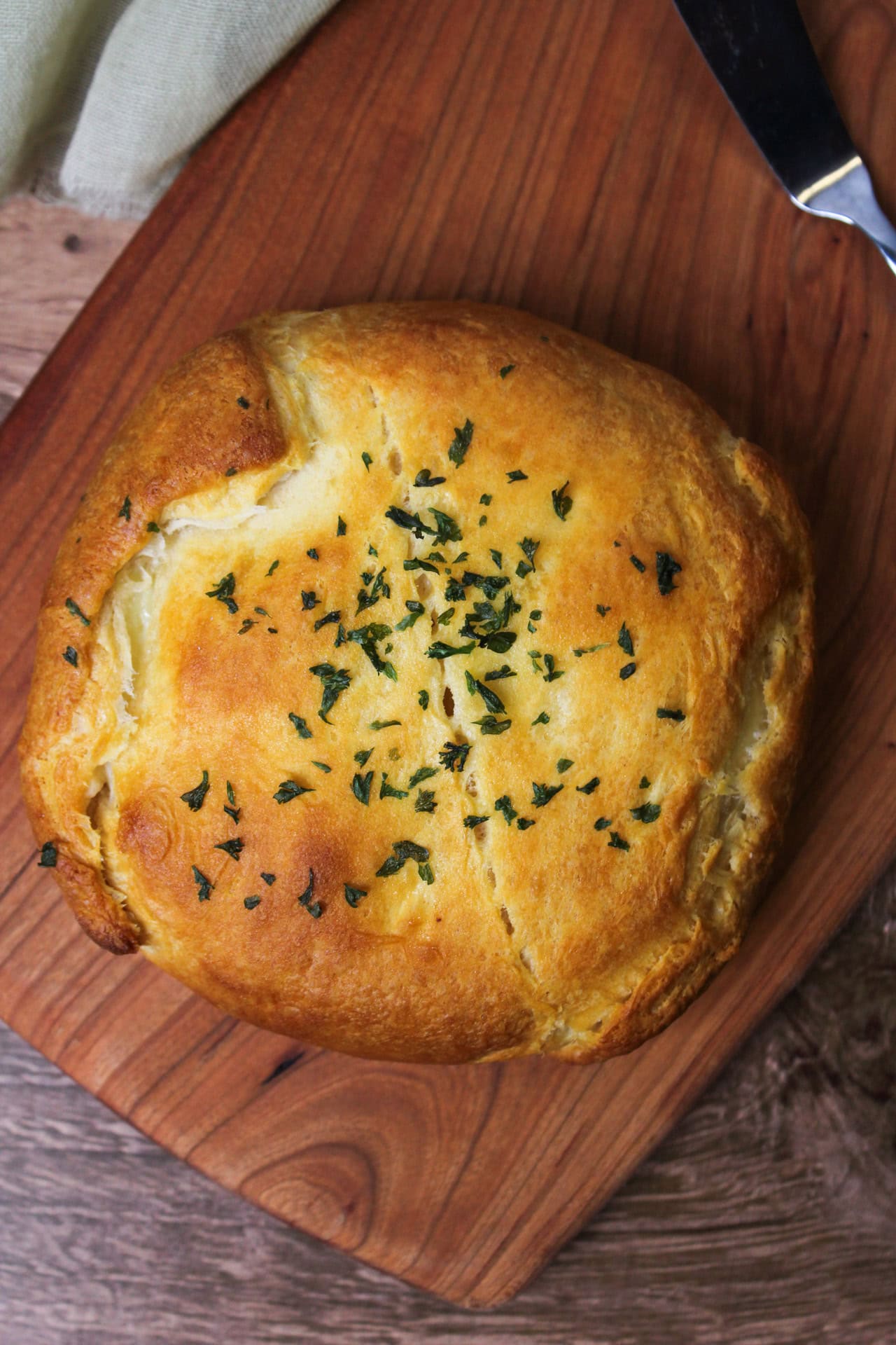 Brie en croute made with crescent roll dough topped with dried parsley on a wooden serving board.