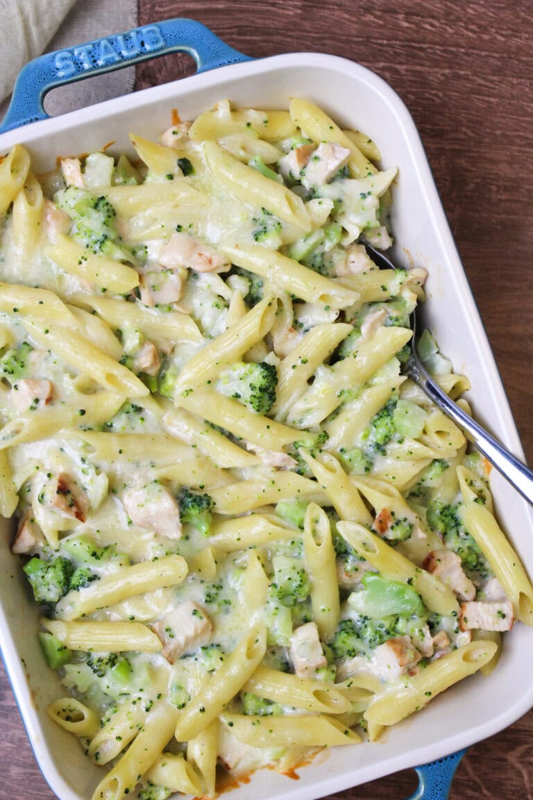 A creamy, cheesy chicken broccoli pasta bake in a blue ceramic baking dish with a serving spoon.