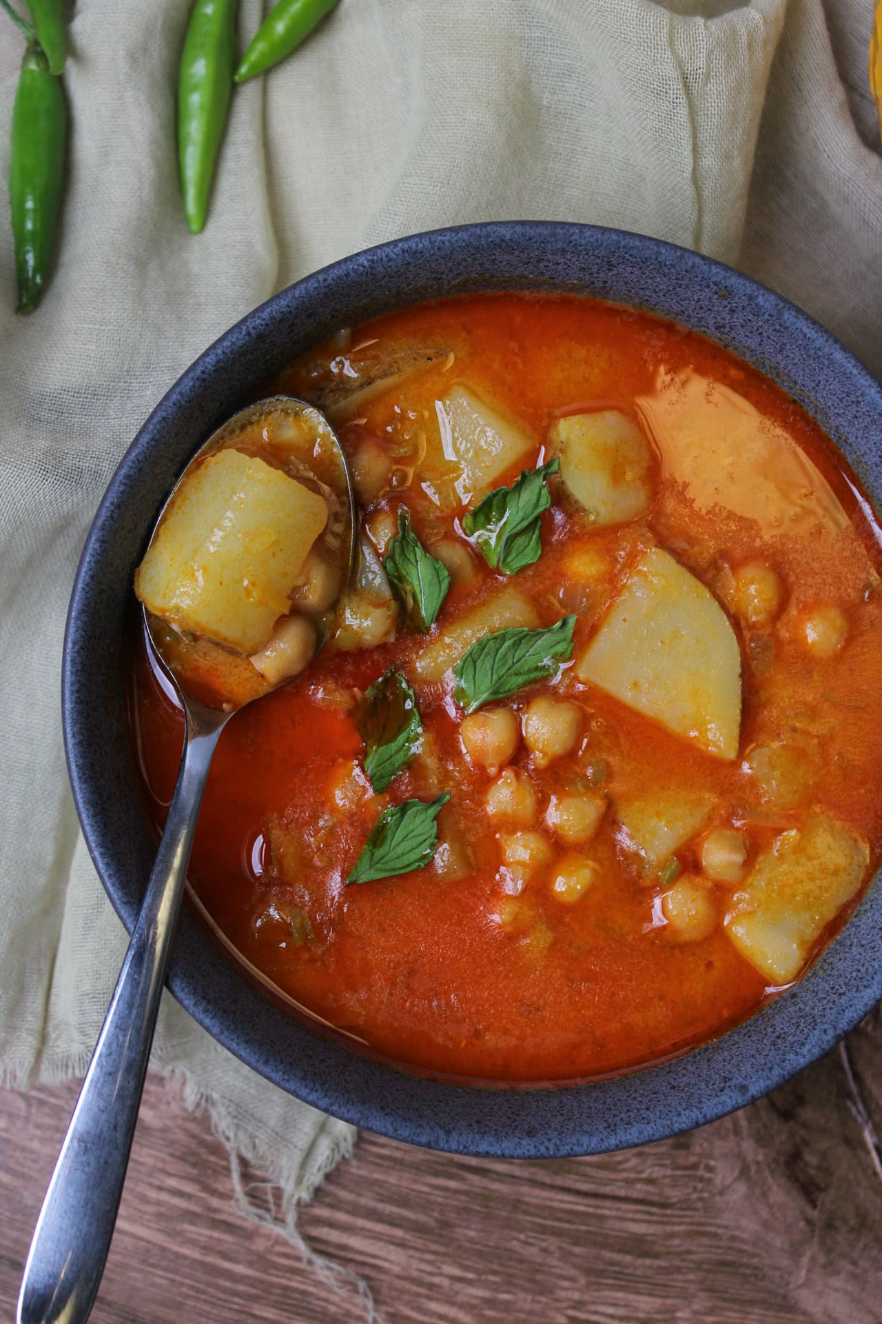 Chickpea potato Thai curry garnished with mint leaves in a blue stone bowl.