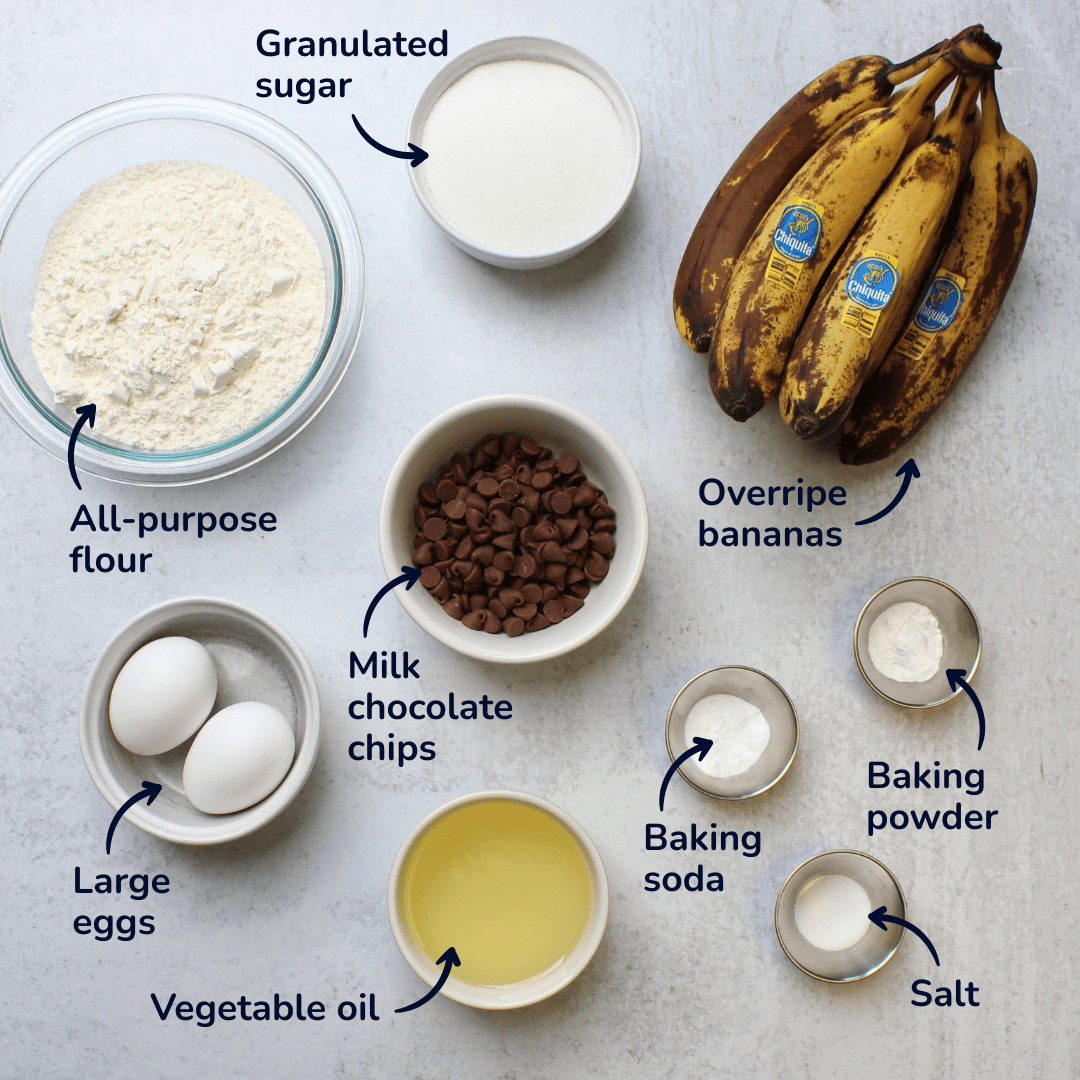 Ingredients for chocolate chip banana bread: overripe bananas, sugar, flour, milk chocolate chips, eggs, vegetable oil, baking soda, baking powder, and salt.