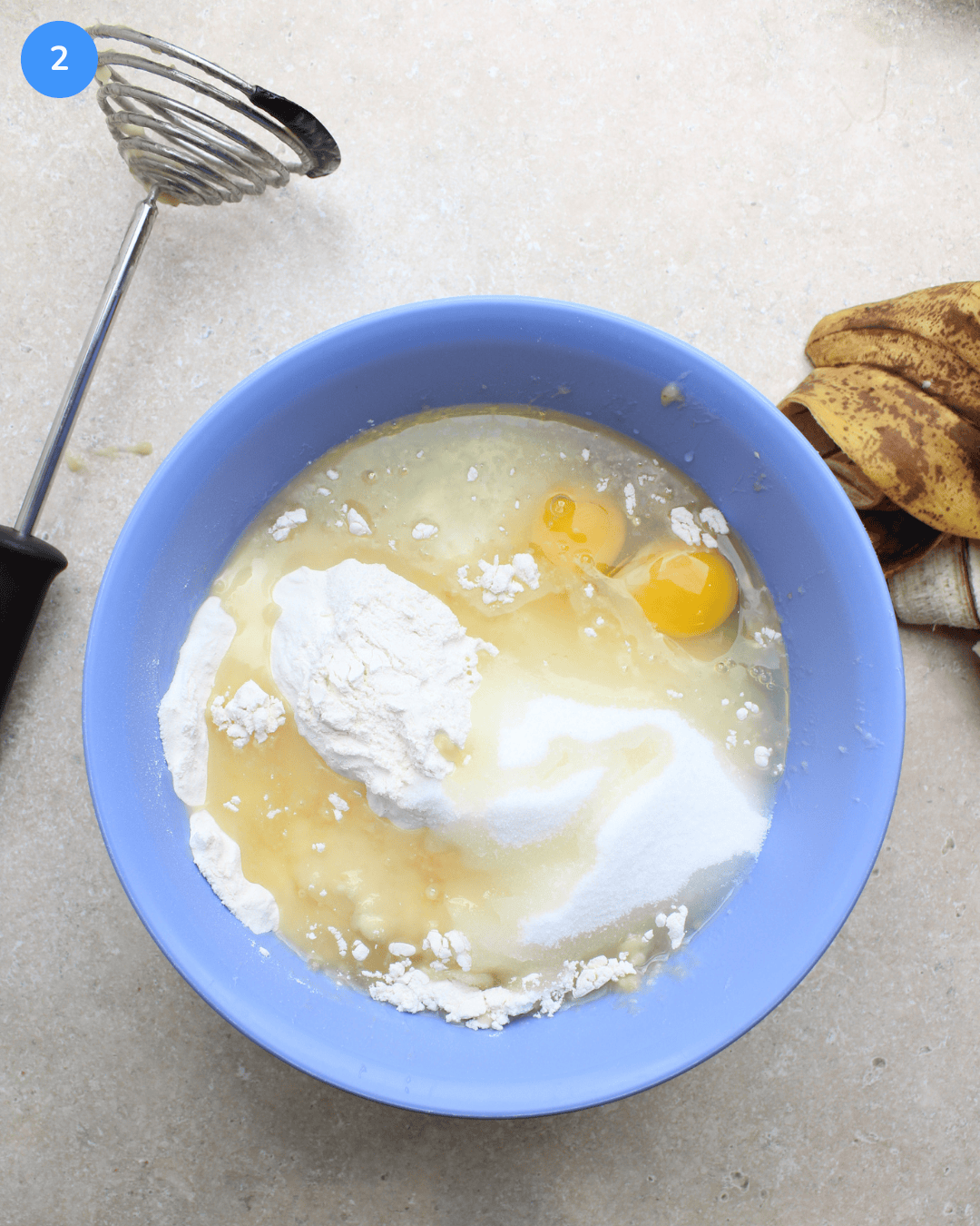 Flour, sugar, eggs, oil, and mashed banana in a blue mixing bowl.