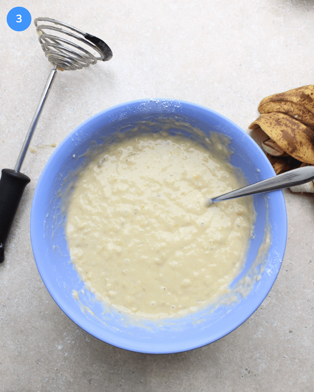 A blue mixing bowl with banana bread batter and a spoon in it.