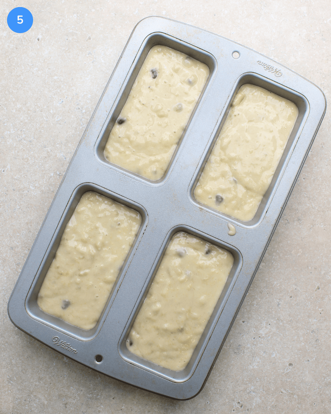 A mini loaf pan with four wells filled with chocolate chip banana bread batter.