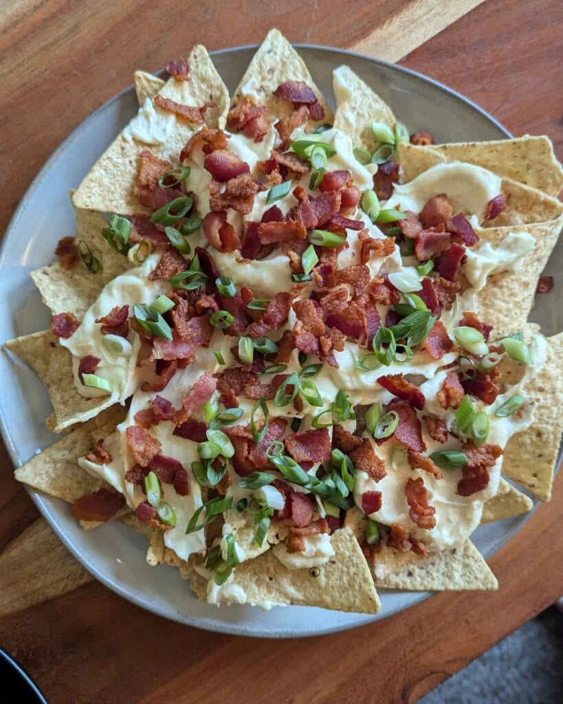 A plate of nachos topped with creamy beer cheese sauce, crumbled bacon, and fresh scallions.