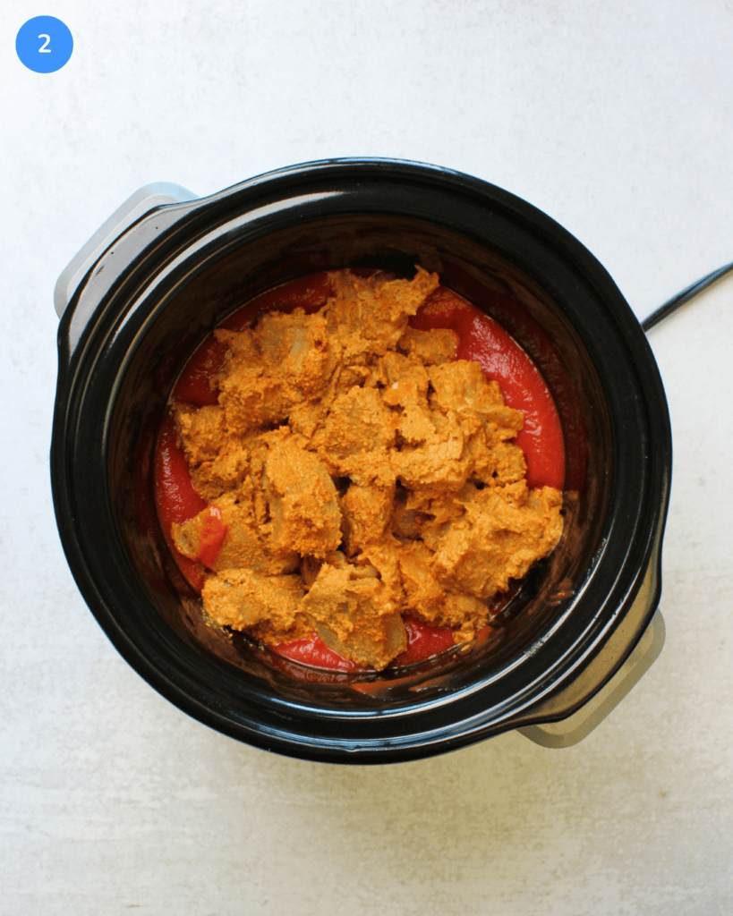 A black slow cooker with marinated chicken tikka masala and tomato puree in it.
