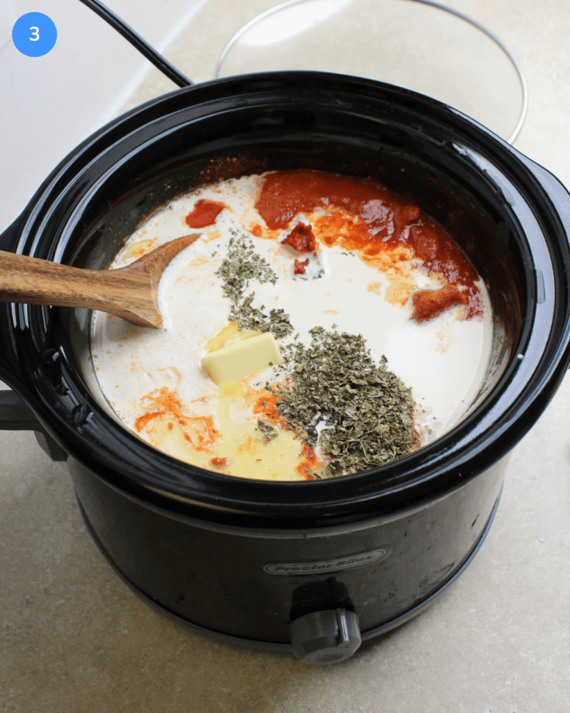 A black slow cooker filled with chicken tikka masala, tomatoes, heavy cream, butter, and fenugreek leaves.